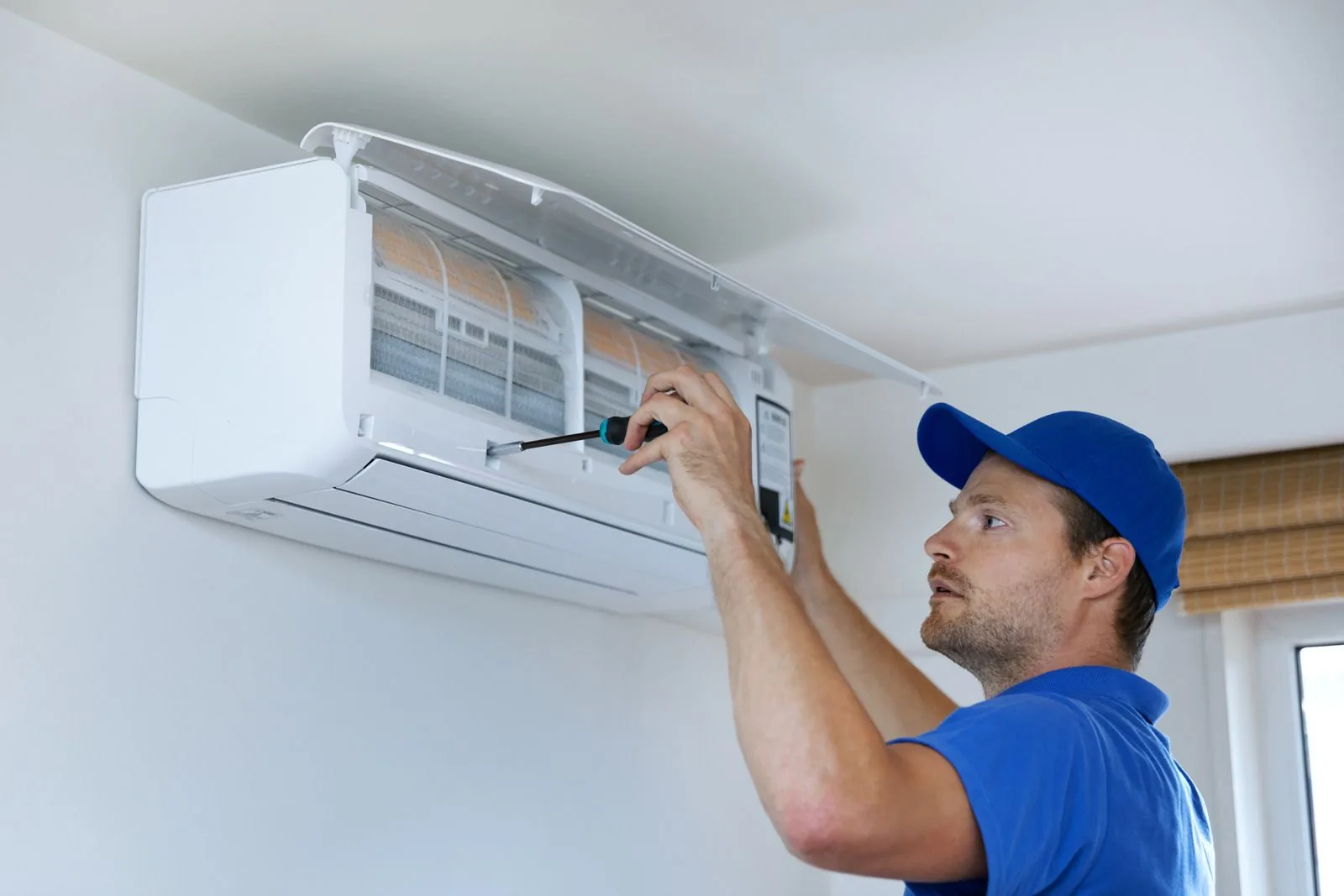 Technician performing maintenance on a wall-mounted air conditioning unit, emphasizing home energy efficiency and comfort during winter.