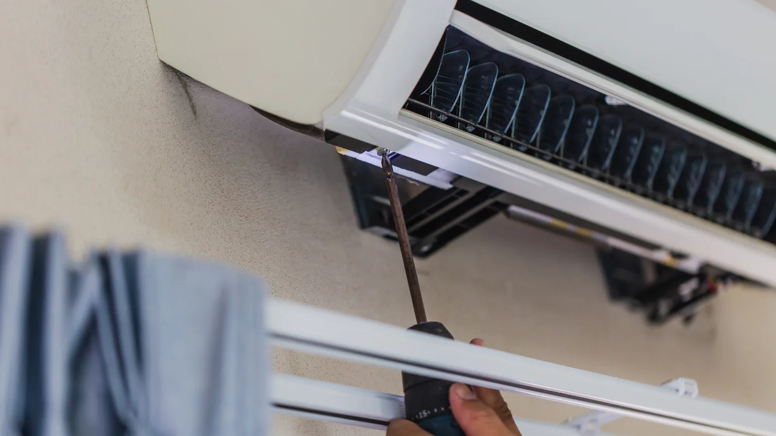 Technician repairing an air conditioning unit with a screwdriver, illustrating AC maintenance and repair services.