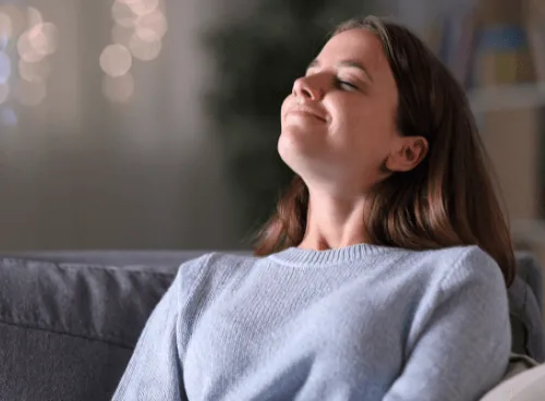Young woman relaxing on a couch, enjoying fresh indoor air, emphasizing the importance of air quality during summer months.