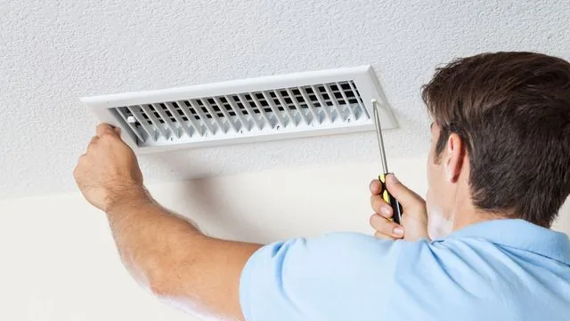 Picture of a man unscrewing an air duct cover in the ceiling.
