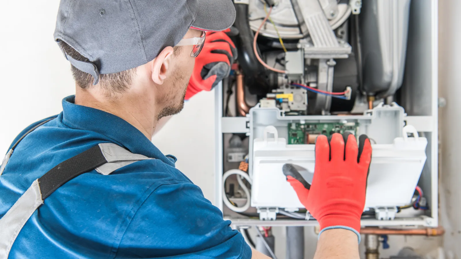 Technician wearing red gloves servicing a furnace, focusing on internal components for HVAC maintenance.