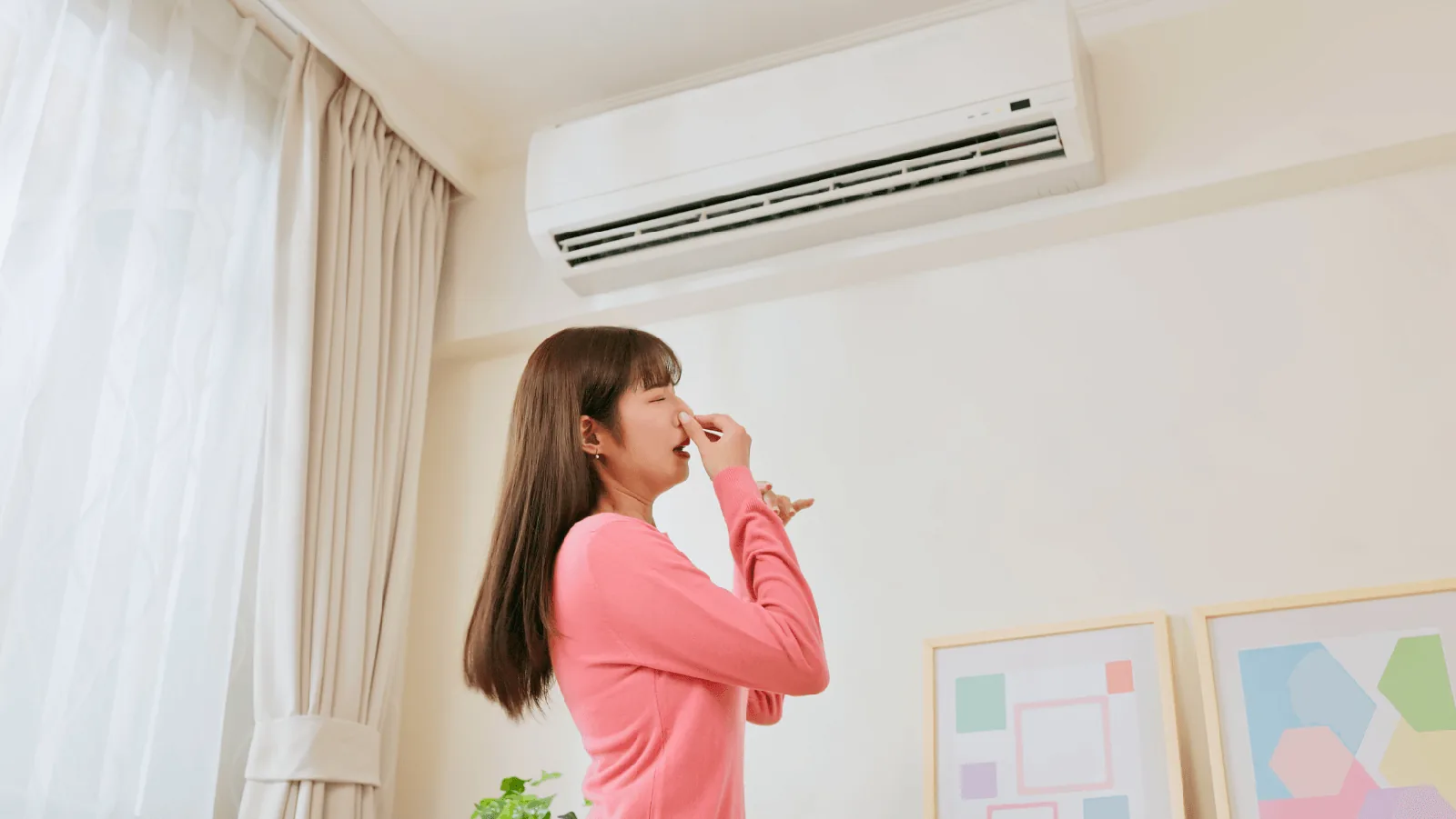 Woman in a pink sweater pinching her nose, reacting to a gas smell indoors