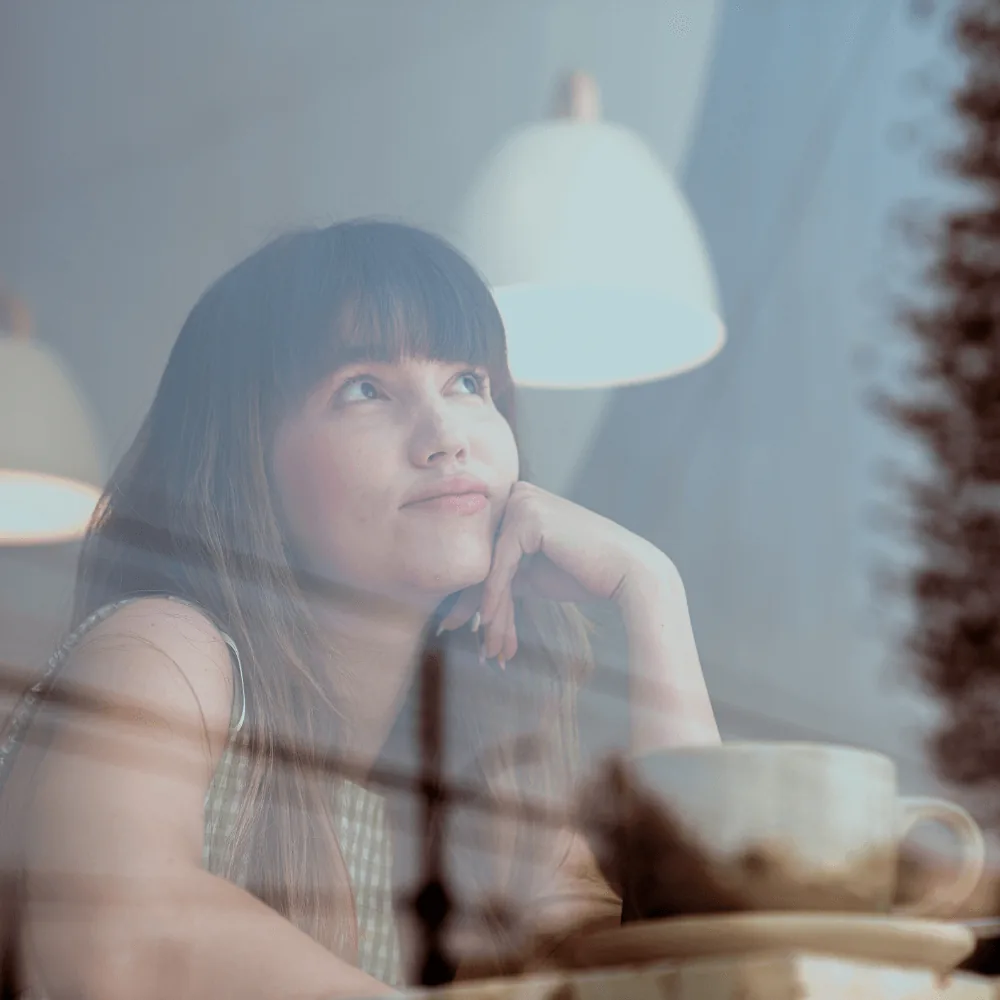 Thoughtful woman gazing upward, seated at a table with a cup, reflecting on heater installation considerations and renewable energy options.