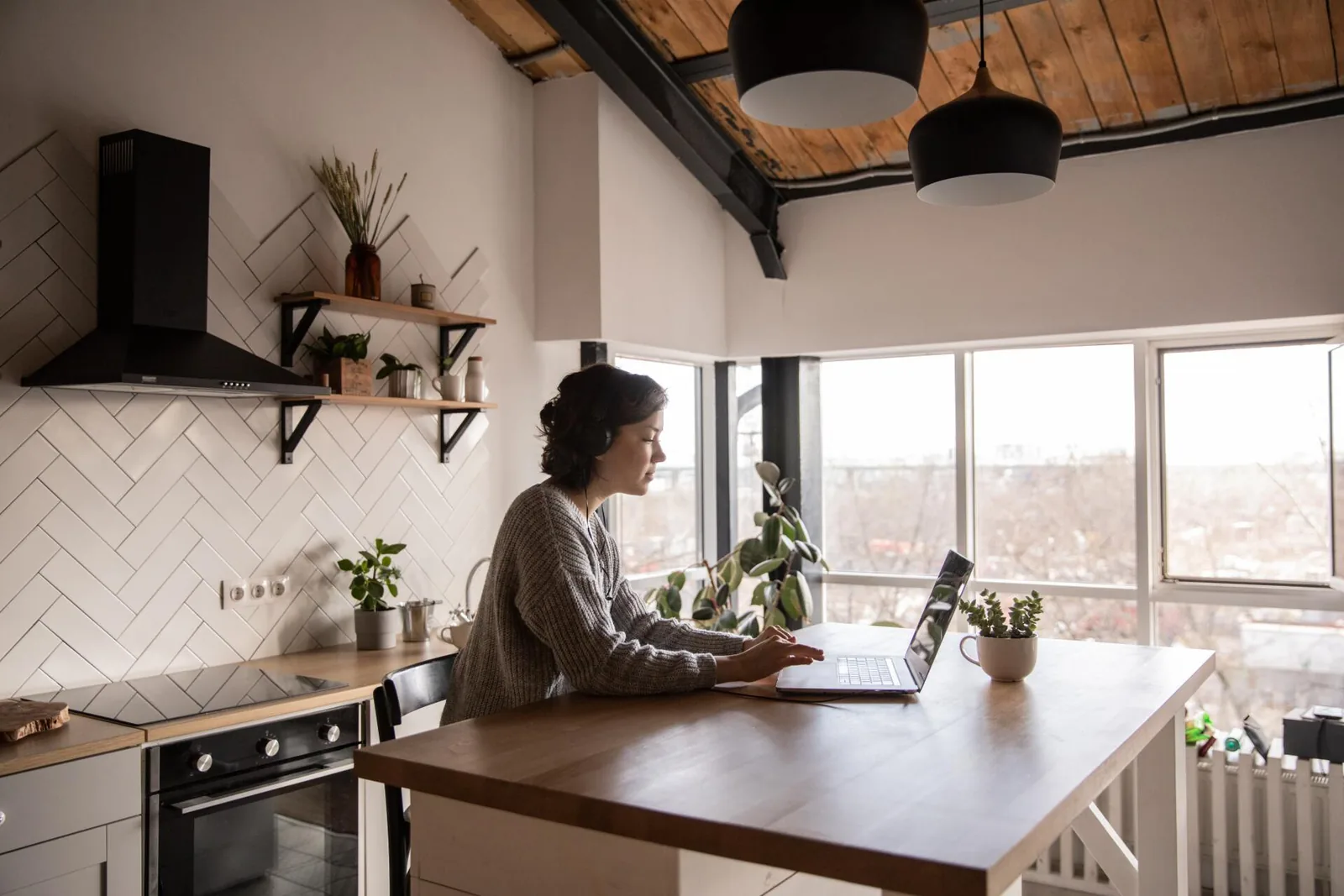 Woman working on laptop at a wooden kitchen table in a modern home