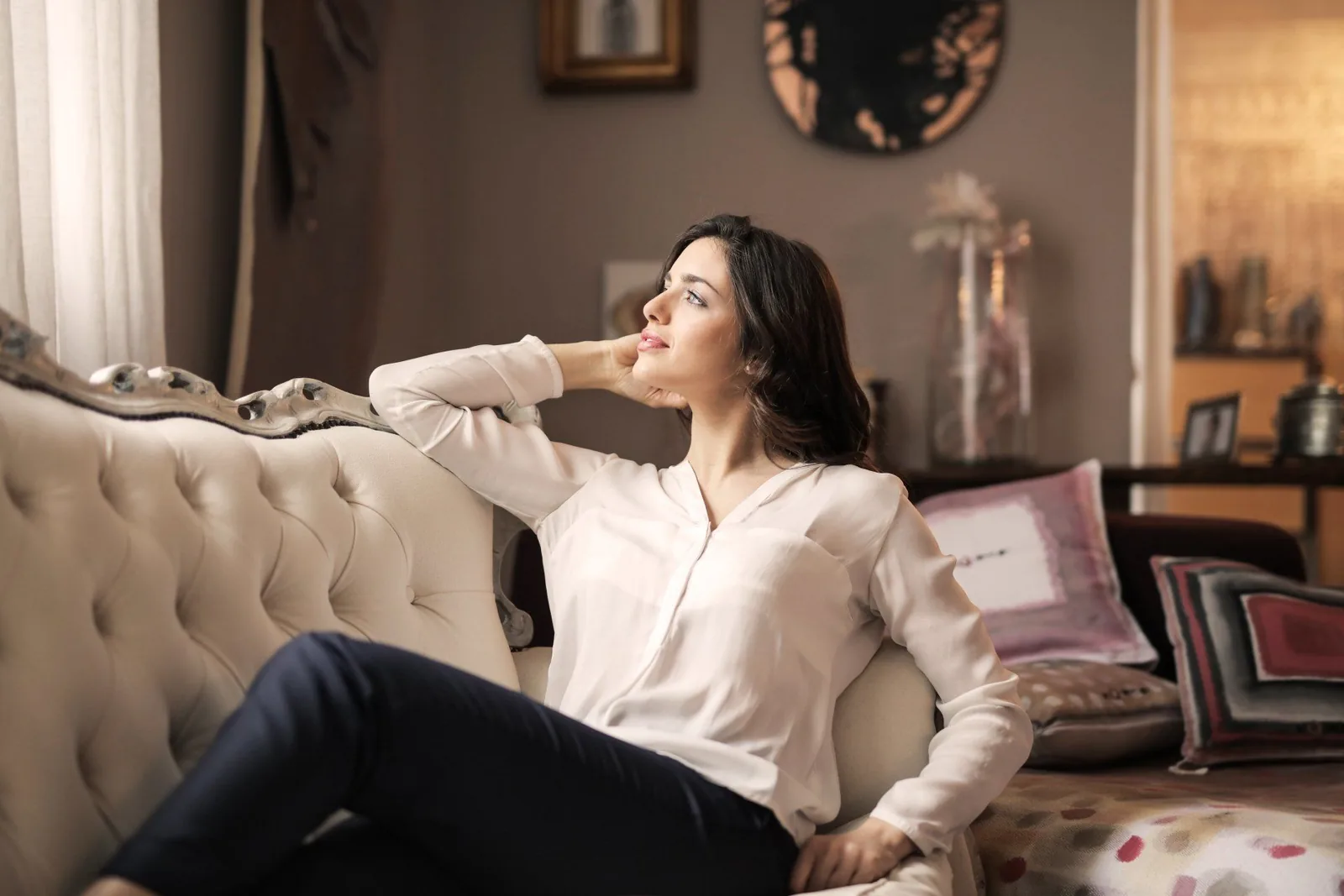 Woman relaxing on a tufted sofa, contemplating comfortably in a cozy indoor setting, emphasizing a serene atmosphere