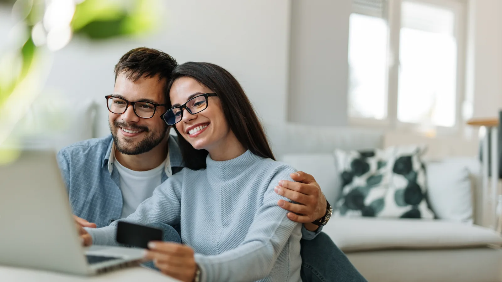 Couple smiling and using a laptop at home, demonstrating comfort and connection while considering HVAC services for