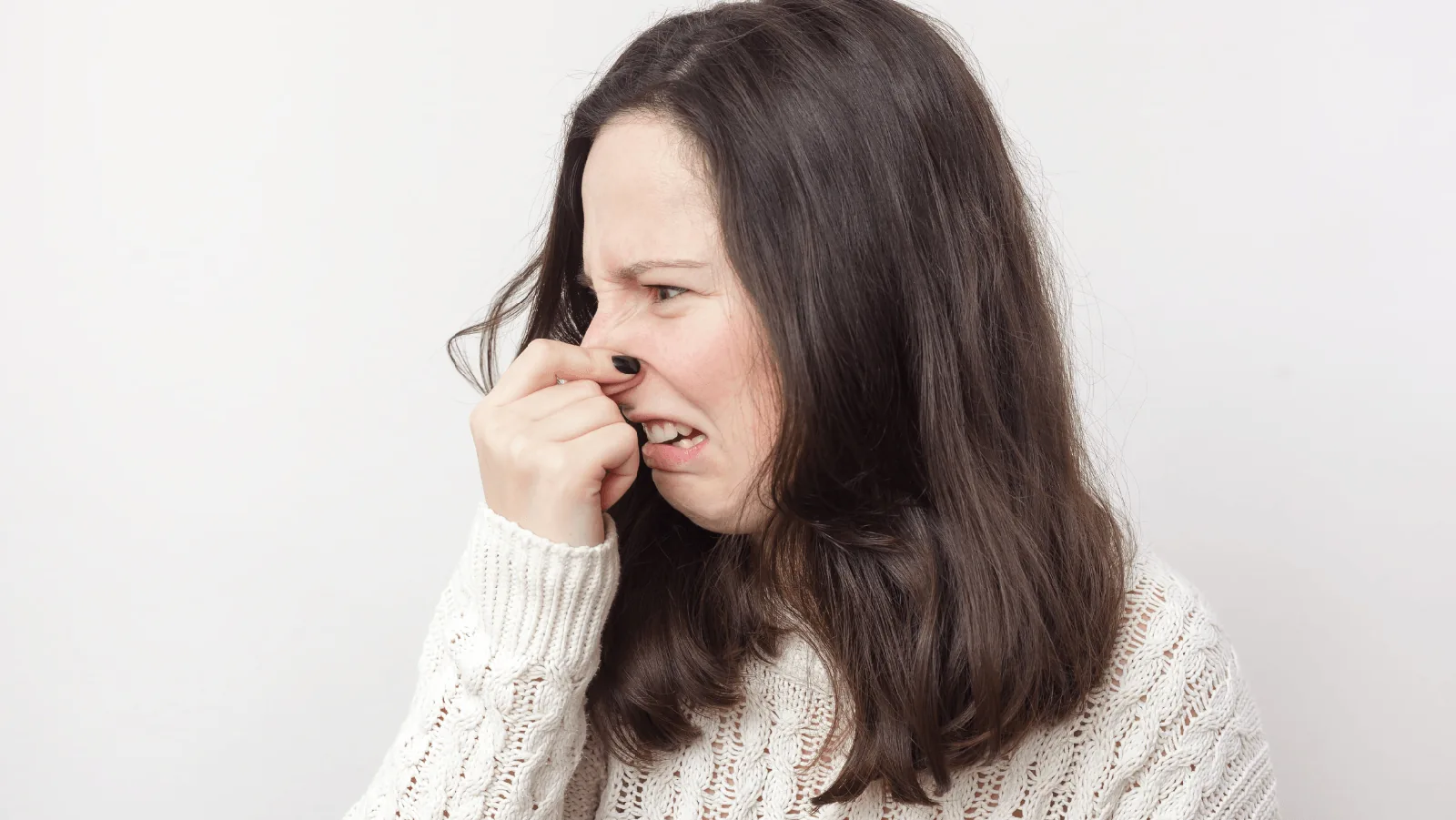 Woman grimacing while pinching her nose, expressing disgust, relevant to HVAC odors and maintenance issues.