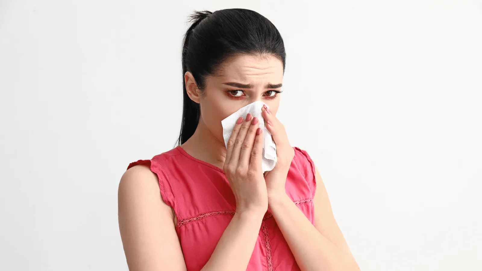 Woman in a pink shirt holding a tissue to her face, showing signs of allergy discomfort, emphasizing the importance of