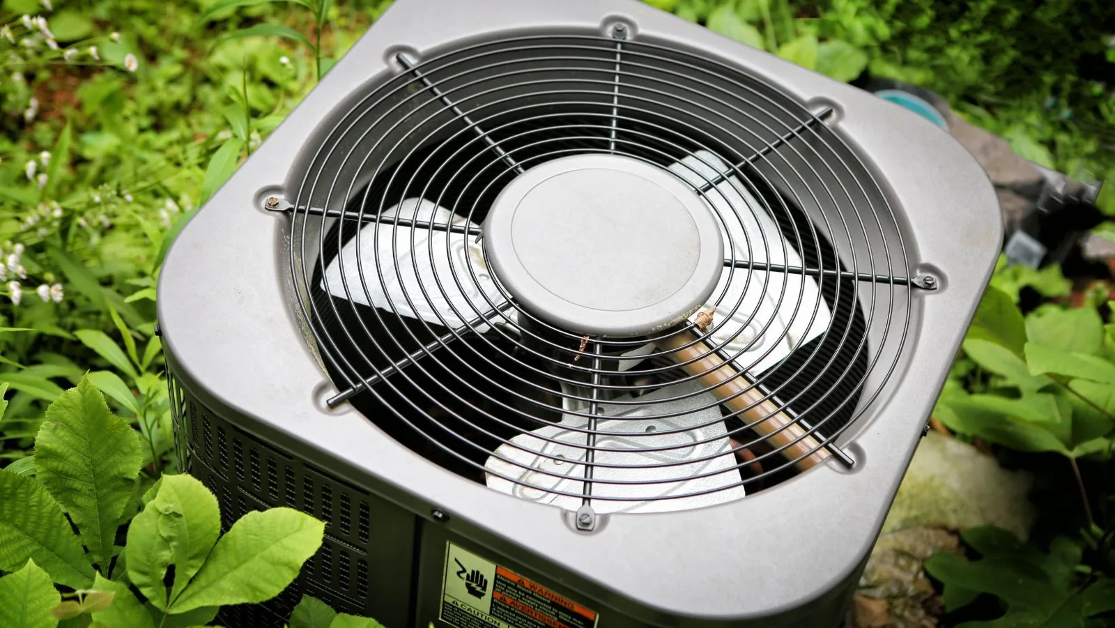 Air conditioner unit with fan and coils surrounded by green foliage, illustrating common HVAC issues related to air conditioning fan operation.