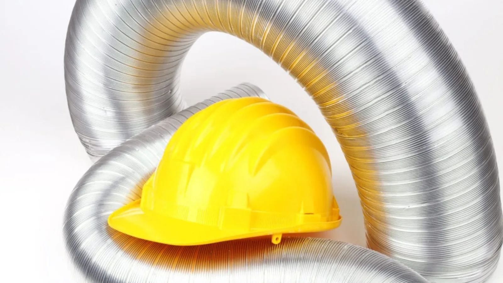 Yellow hard hat resting on flexible metal ductwork, symbolizing HVAC installation and maintenance services.