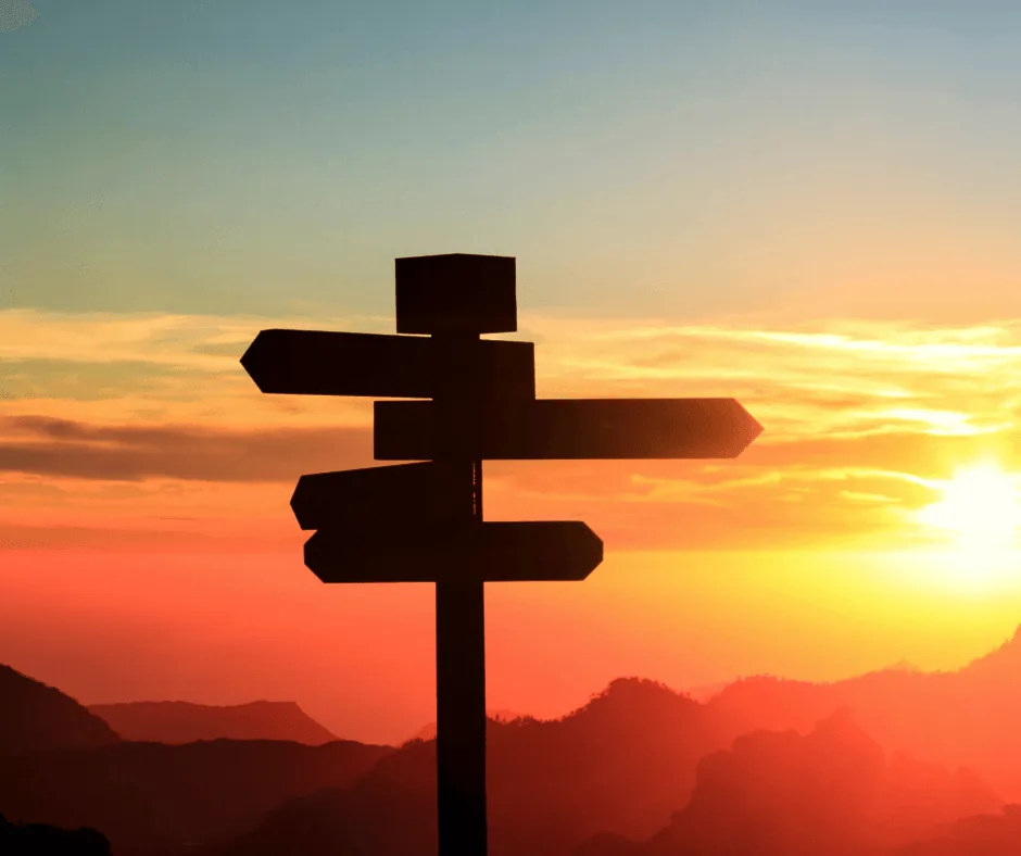 Silhouette of a directional signpost against a vibrant sunset sky, symbolizing choices and guidance in HVAC system replacement decisions.