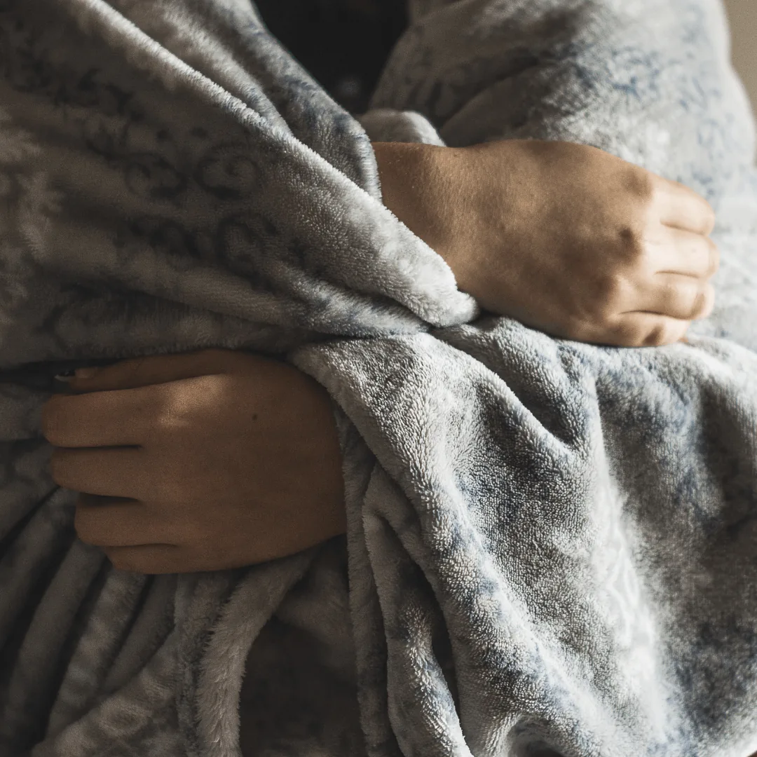 Person wrapped in a cozy gray blanket, emphasizing warmth and comfort during winter, relevant to HVAC tips for efficient