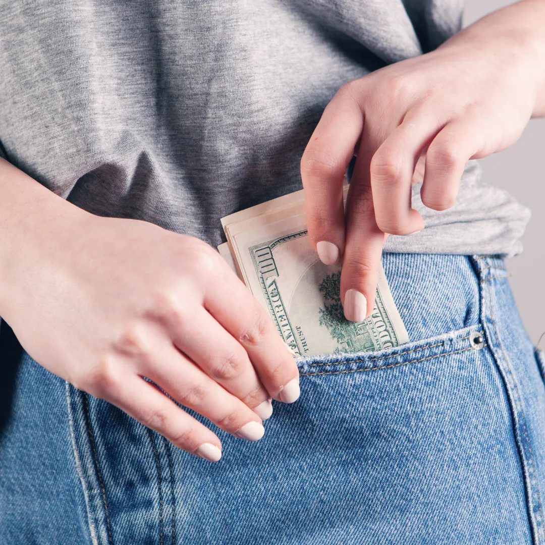 Person placing cash into the back pocket of denim jeans, symbolizing savings and financial management.