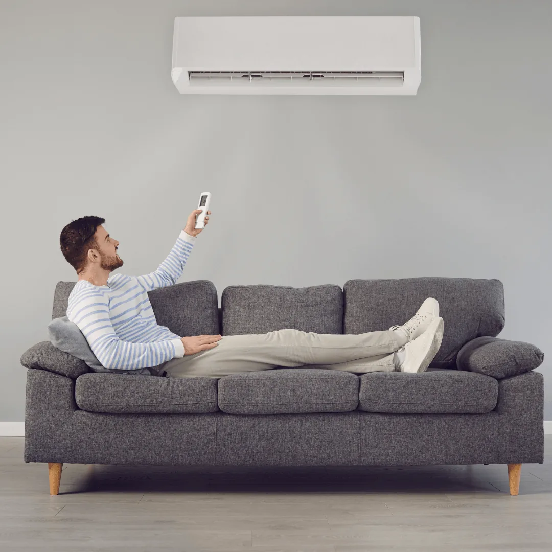 Man relaxing on a couch using a remote control for a ductless mini-split air conditioning unit, emphasizing HVAC comfort