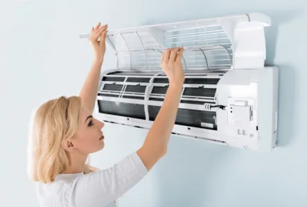 Woman performing maintenance on a wall-mounted air conditioning unit, highlighting the importance of air filter