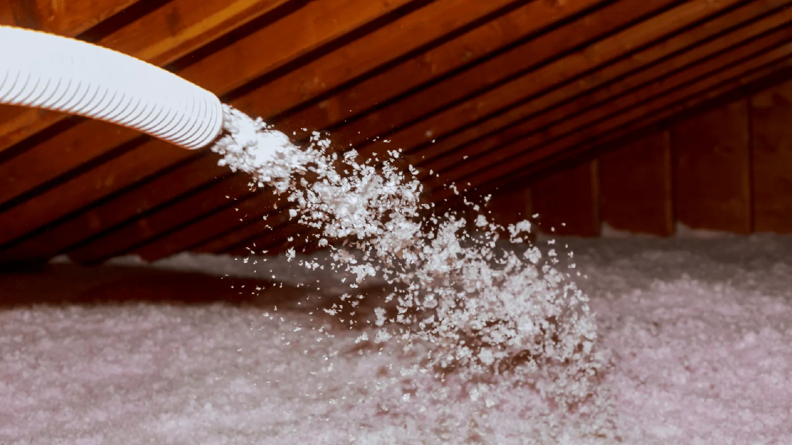 Insulation being blown into an attic space, showcasing the importance of proper insulation for HVAC efficiency and temperature regulation.
