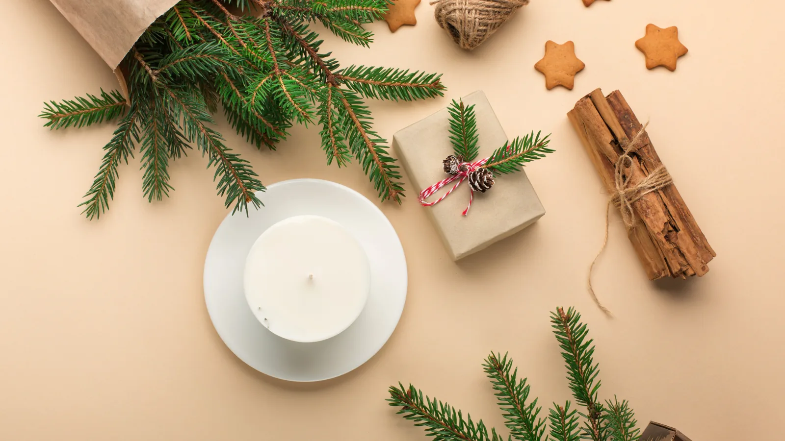 Eco-friendly home fragrance setup featuring a white candle on a plate, fresh pine branches, a wrapped gift