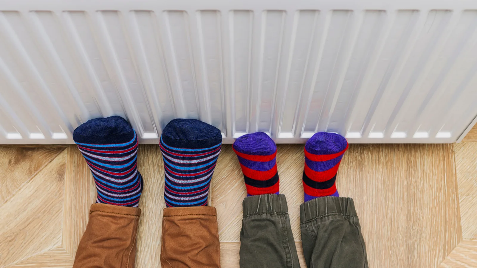 Children's feet in colorful socks warming by a radiator, illustrating the importance of heater functionality during winter.