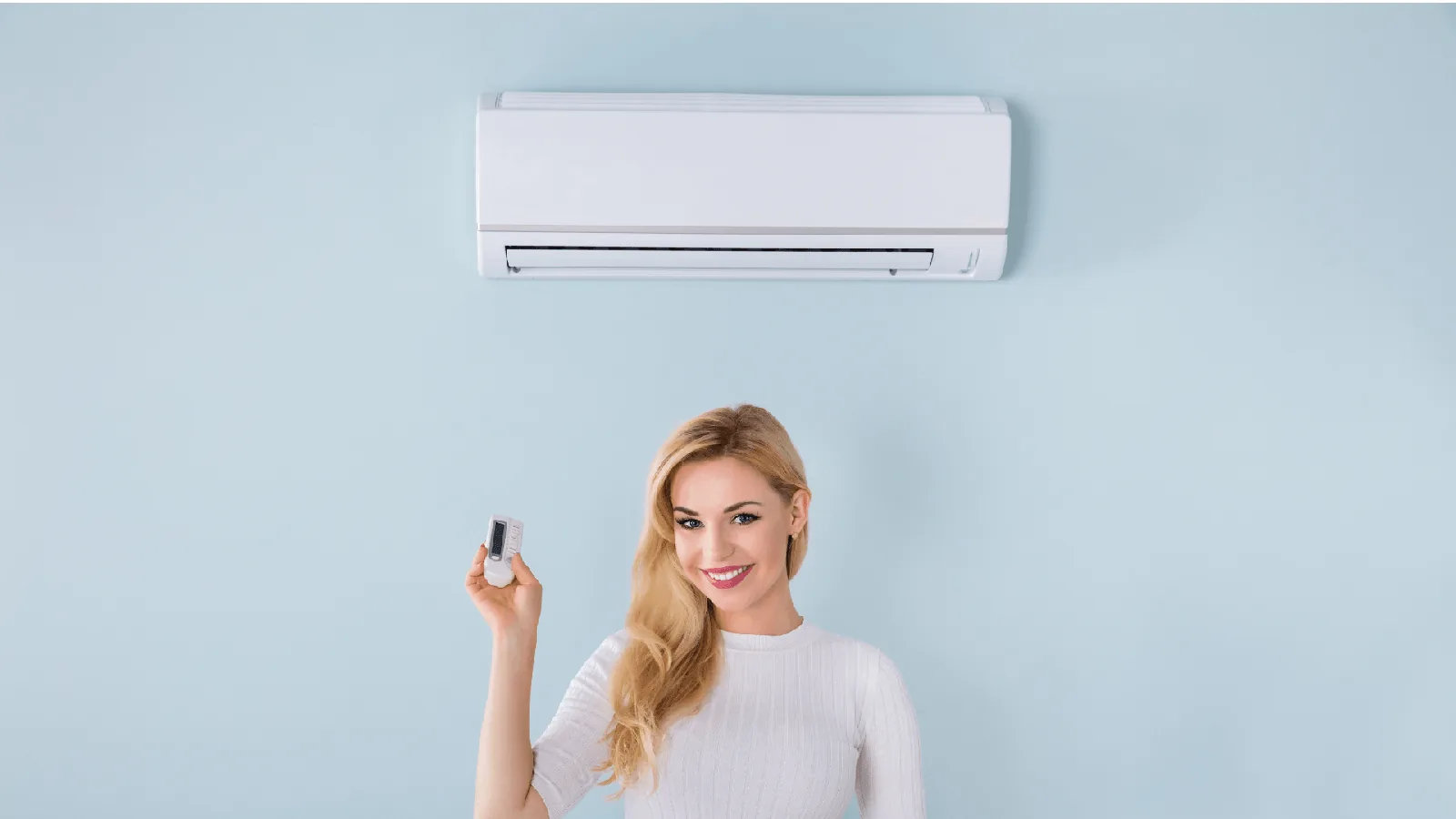 Woman holding remote control for ductless mini-split air conditioning unit mounted on light blue wall, illustrating HVAC