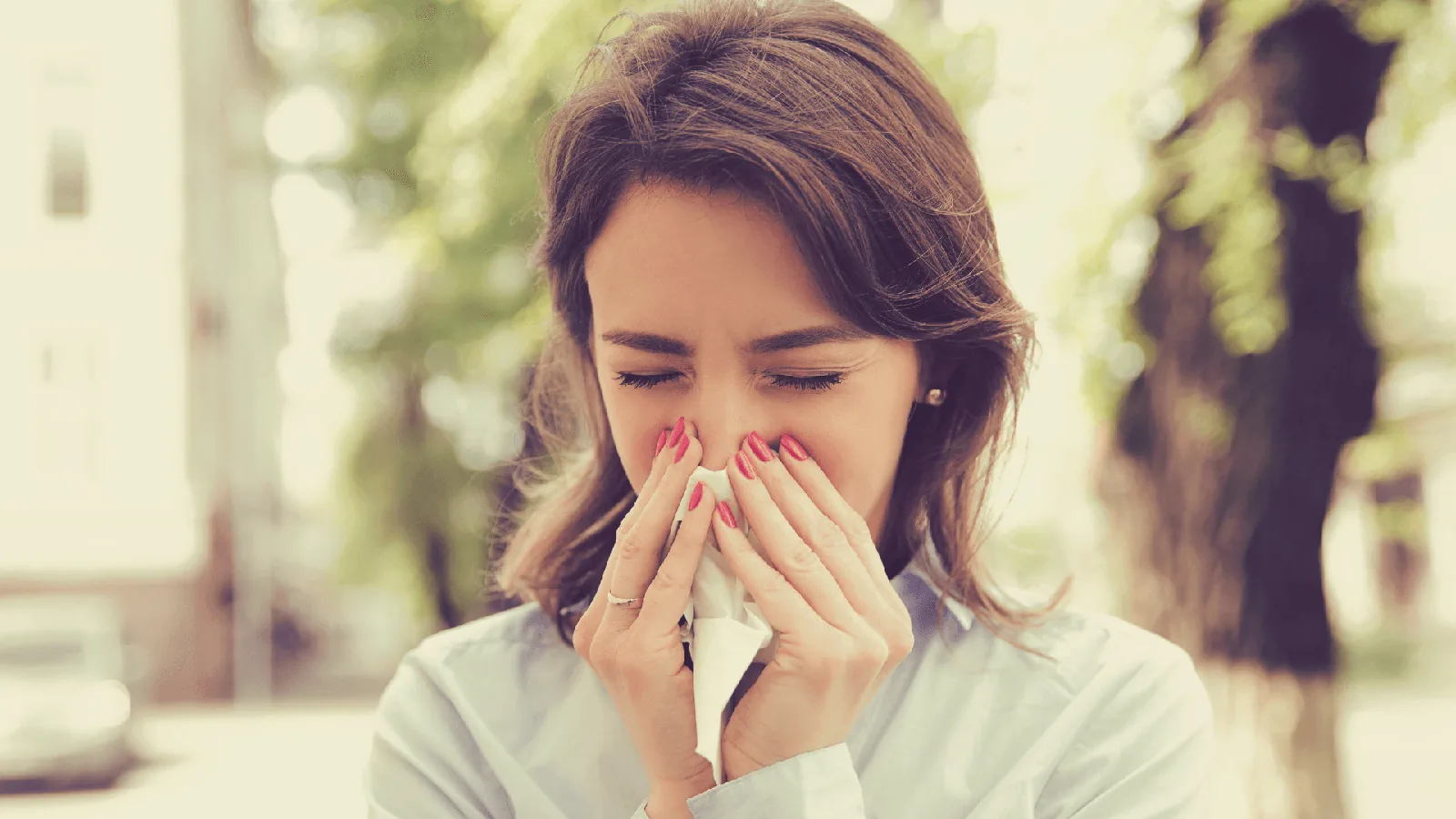 Woman sneezing and holding tissue outdoors, illustrating the impact of allergens and the importance of HVAC systems in improving indoor air quality.