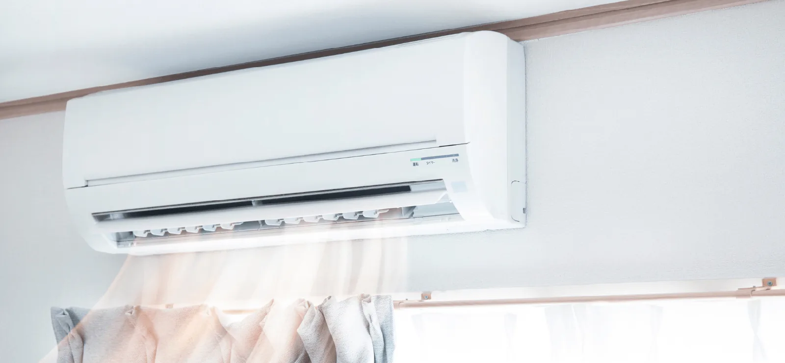 Air conditioning unit mounted on the wall, blowing cool air towards a window