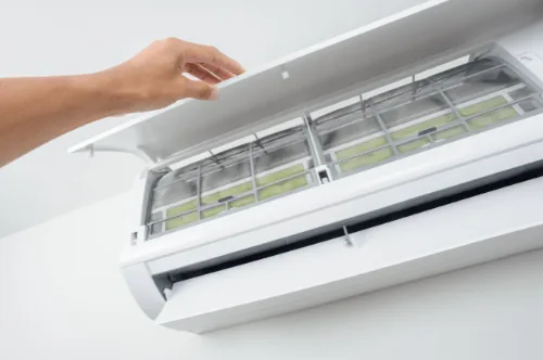 Hand opening the cover of an HVAC unit to access and clean the air filters for improved indoor air quality and system efficiency.