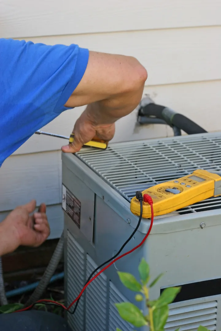 Technician repairing air conditioner unit with screwdriver and multimeter, emphasizing HVAC maintenance services for optimal performance.