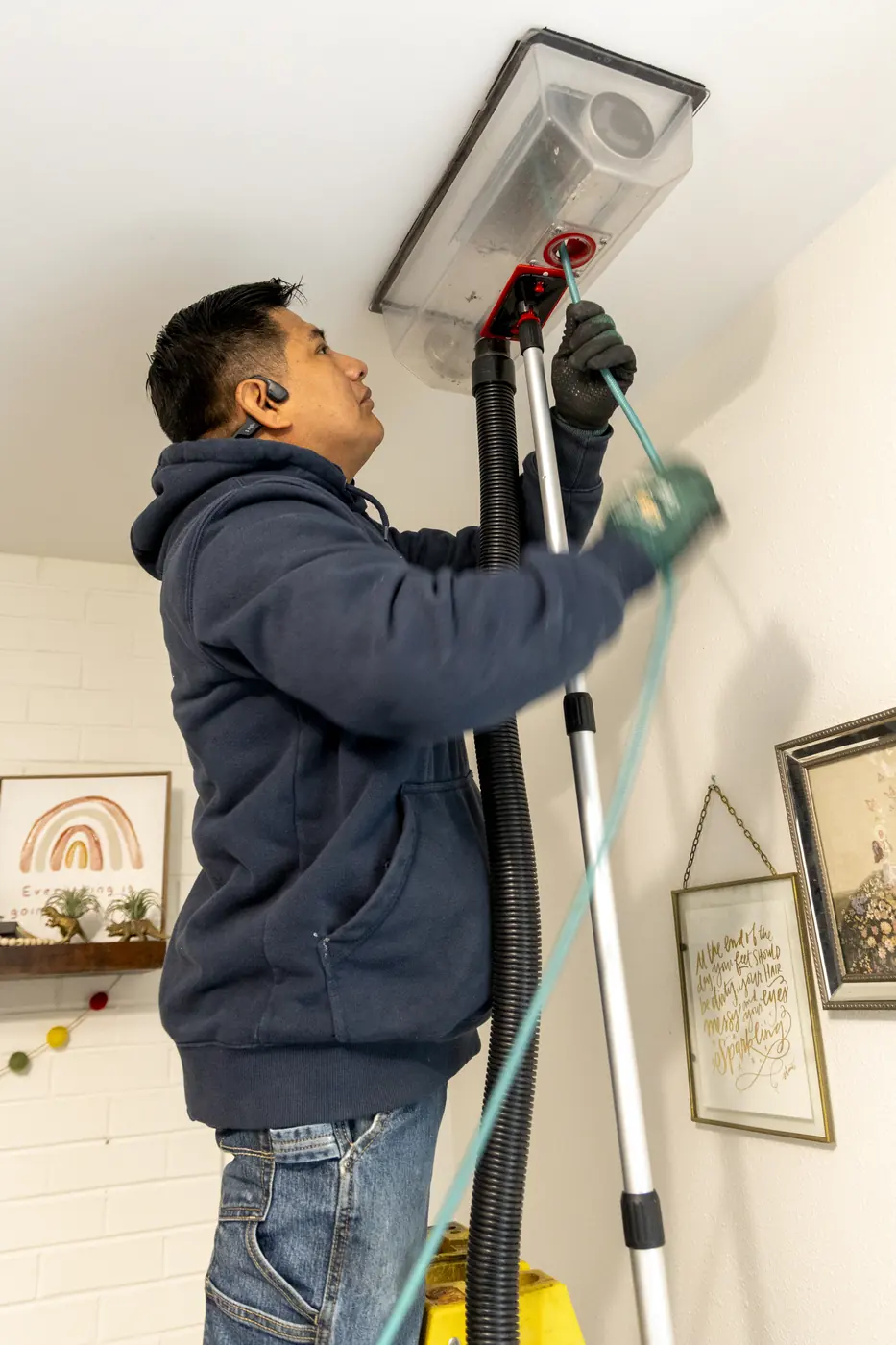 Technician cleaning a ceiling vent with a vacuum hood