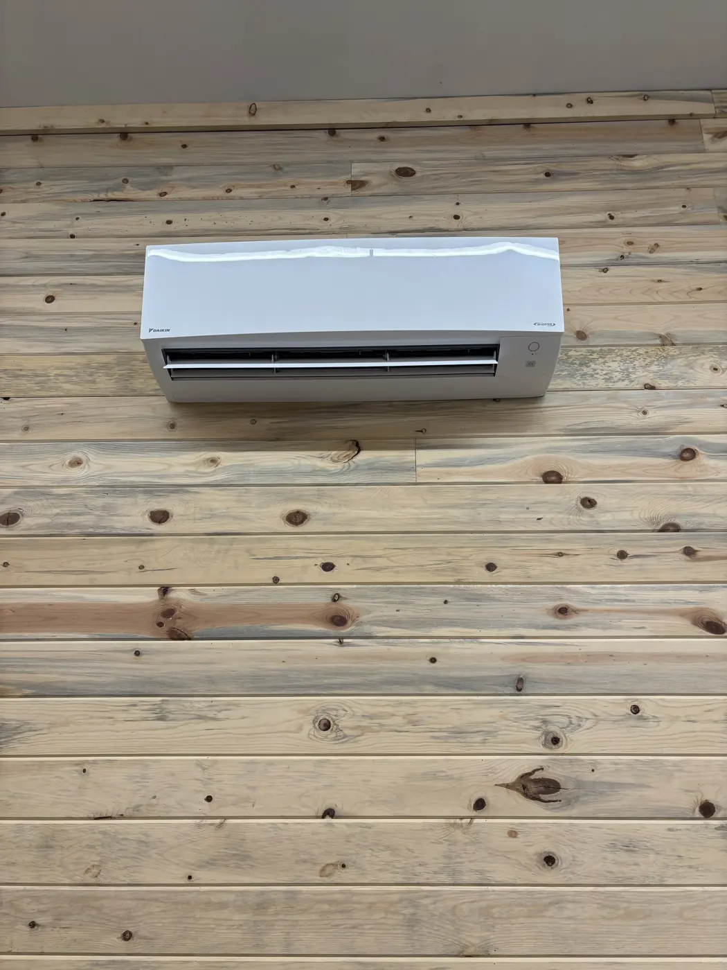 Newly installed ductless mini-split indoor unit on a wood-plank wall